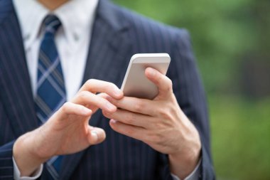 Bir iş bölgesinin caddesinde akıllı telefon kullanarak iletişim kuran Asyalı bir işadamı