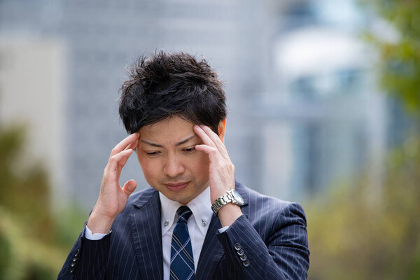 Asian business person suffering from headache due to stress in business