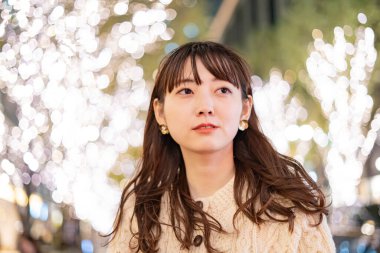 Bir Asyalı (Japon) genç bir kadın gece şehrini renklendiren aydınlatmaları izliyor.