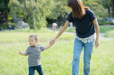 İki yaşındaki çocuk ve annesi güneşli bir günde parkta oynuyorlar.