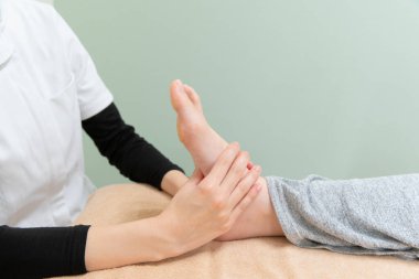 Asyalı kadın pratisyen kadın bir hastanın ayağına ve tabanına masaj yapıyor.