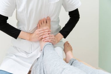 Asyalı kadın pratisyen kadın bir hastanın ayağına ve tabanına masaj yapıyor.