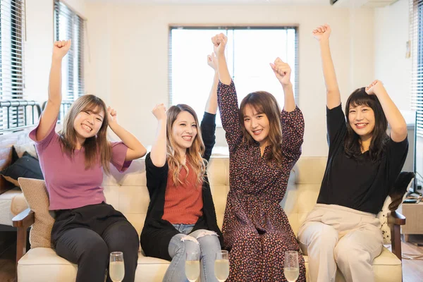 Four Asian young women watching TV indoor and posing cheering