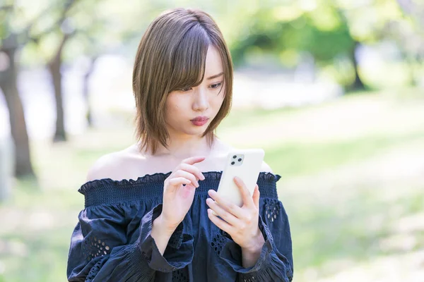 アジアの若い女性が屋外で スマートフォンの画面と操作を見て — ストック写真