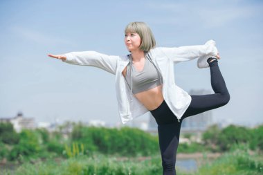 Asyalı genç kadın yeşil alanda esneme egzersizi yapıyor.