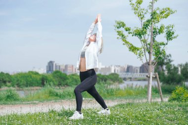 Asyalı genç kadın yeşil alanda esneme egzersizi yapıyor.