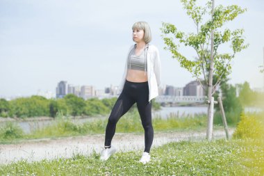 Asyalı genç kadın yeşil alanda esneme egzersizi yapıyor.