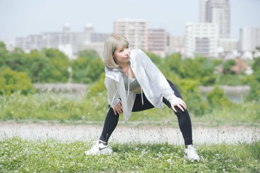 Asyalı genç kadın yeşil alanda esneme egzersizi yapıyor.