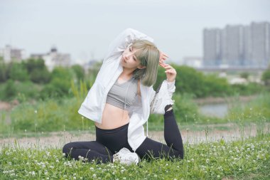 Asyalı genç kadın yeşil alanda esneme egzersizi yapıyor.