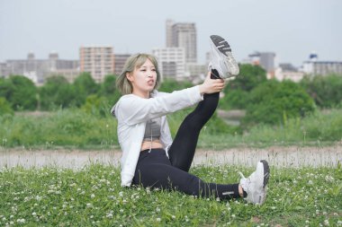 Asyalı genç kadın yeşil alanda esneme egzersizi yapıyor.