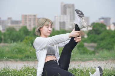 Asyalı genç kadın yeşil alanda esneme egzersizi yapıyor.