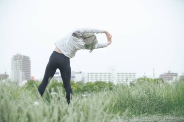 Asyalı genç kadın yeşil alanda esneme egzersizi yapıyor.