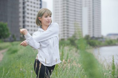 Asyalı genç kadın yeşil alanda esneme egzersizi yapıyor.