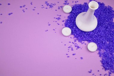 Mumlar ve deniz banyosu tuzu. Rahatlamak için lavanta. Pembe arka planda büyük lavantalı deniz banyosu tuzu serpilmiştir. Kokulu mumlar ve resmin köşesinde beyaz bir vazo. Arkaplanın yarısı metin için boş.
