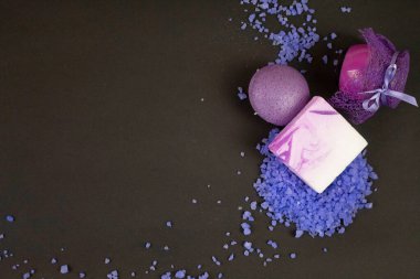 Siyah arka planda leylak renginde düz yatıyordu. SPA için hazır: lavanta banyosu tuzu, cam şişedeki kokulu mum, yumuşak cilt bakımı için sünger. Violet ruh hali, rahatlama, güzellik ve özen dolu.