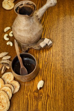 Kahve, kurabiye ve fındık. Halk tarzında seramik kahve seti yakın plan. Ardıç tutacağı ve kaşık kahve. Choux ve mısır gevreği kurabiyeleri ve esmer şeker küpleri. Sıcak renklerde kompozisyon.