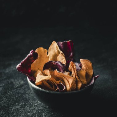 Siyah arka planda siyah kase, pancar kökü, tatlı patates ve havuç cipsi ile fotokopi alanı.