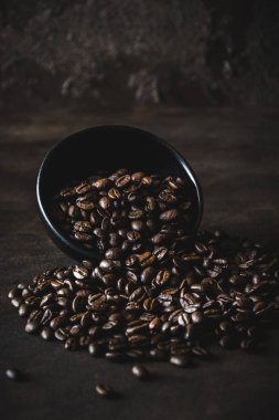 Kahve çekirdekleri aşağı doğru eğimli siyah kaseden ön plana doğru, koyu kahverengi arka plan, karamsar atmosfer
