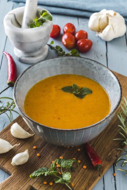 Gri bir masanın üzerinde bitkiler, domatesler, biberler ve sarımsaklı lezzetli renkli mercimek kreması çorbası var.