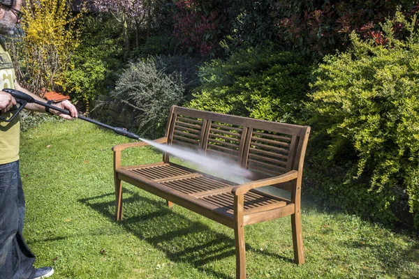 Man cleaning wooden garden bench with a high pressure cleaner in spring time.