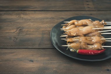 Çiğ tavuk şişi ve koyu ahşap üzerine kırmızı biber tabağı. Boşluğu kopyala.