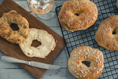 Gri ahşapta soğutucu rafında ev yapımı simit. Tahtada tereyağı, bir bardak şarap. Üst görünüm.