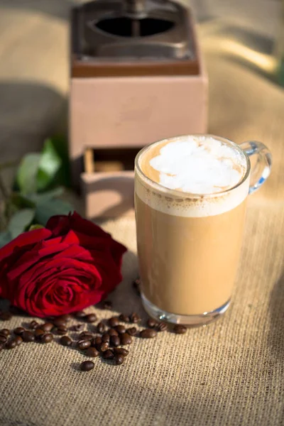 Latte macchiato com rosa vermelha e moinho de café no fundo — Fotografia de Stock