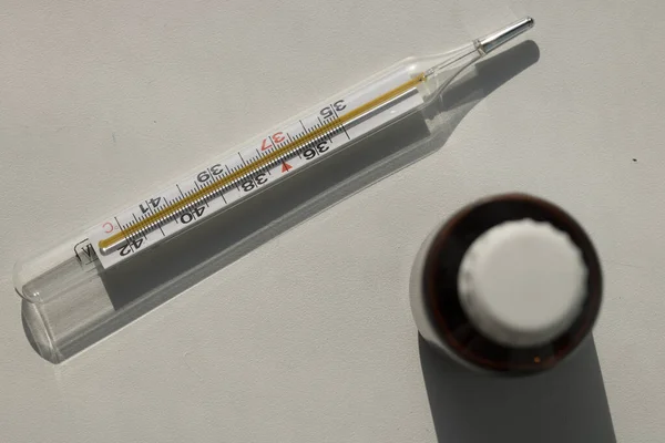 Beyaz arka planda ilaç şişesi olan termometre.