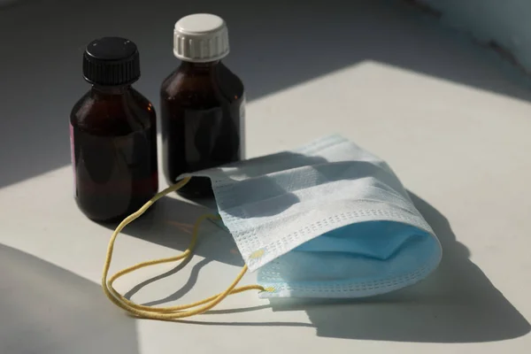 Beyaz arka planda tıbbi şişeleri olan mavi tıbbi maske.