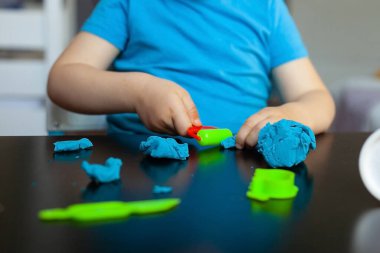 Odanda renkli kil kalıplarıyla oynayan çocuk evde küçük bir çocuk heykeli yapıyor. Anaokulu çocukları için eğitici oyunlar