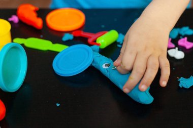 Odanda renkli kil kalıplarıyla oynayan çocuk evde küçük bir çocuk heykeli yapıyor. Anaokulu çocukları için eğitici oyunlar