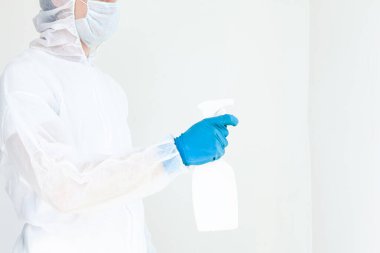 Koruyucu giysili eldiven ve maske takmış elinde sprey tutan bir adam. Antibakteriyel tedavi kavramı. Beyaz bir arkaplanda izole edilmiş
