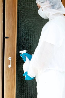 Koruyucu giysili eldiven ve maske takmış elinde sprey tutan bir adam. Halka açık bir yerde antibakteriyel tedavi kavramı