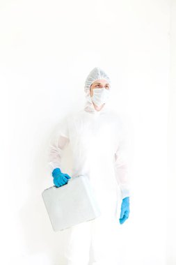 Koruyucu takım elbiseli, eldivenli ve maskeli bir adam elinde bir bavulla elinde testler için yürüyor. Koronavirüsle mücadele kavramı. Beyaz bir arkaplanda izole edilmiş
