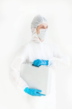 Koruyucu takım elbiseli, eldivenli ve maskeli bir adam elinde bir bavulla elinde testler için yürüyor. Koronavirüsle mücadele kavramı. Beyaz bir arkaplanda izole edilmiş
