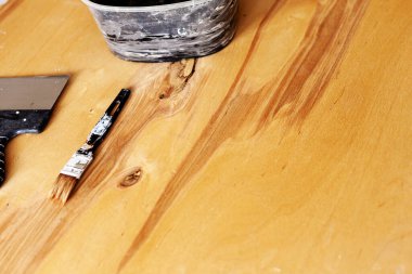 Tahta bir paneli boyama süreci. Fırça ve spatula ahşap yüzeyde yatıyor.