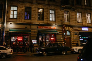 Gece sokağı. Geniş pencereli restoran. Yolun kenarına antik bir GAZ-21 park edilmiş. Gece hayatı ve eğlence anlayışı