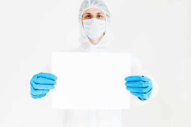 Koruyucu giysili, eldivenli ve maskeli bir adam elinde bir işaret tutuyor. Beyaz bir arkaplanda izole edilmiş