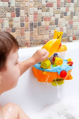 Bir çocuk köpük banyosunda banyo yapıyor. Bir çocuk tuvalet için oyuncaklarla oynuyor.
