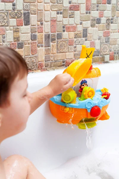 Bir çocuk köpük banyosunda banyo yapıyor. Bir çocuk tuvalet için oyuncaklarla oynuyor.