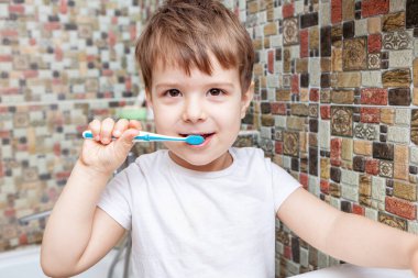 Diş fırçasıyla dişlerini fırçalayan çocuğun yakın çekimi. Mutlu çocuk banyo odasında küçük dişlerini fırçalıyor. Sağlıklı küçük çocuğun portresi mutlu bir yüzle dişlerini temizlemekten zevk alır. Diş Konsepti