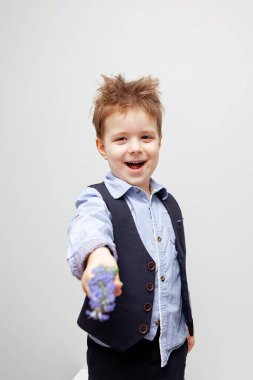 Gömlek, yelek ve pantolon giymiş bir çocuk elinde bir çiçek tutuyor. Beyaz arkaplan