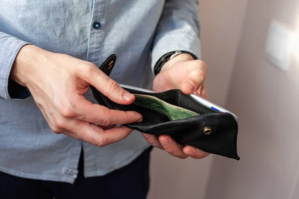 A man in a denim shirt holds a wallet. Men's hands and take out or put a $ 2 bill in the wallet. The concept of poverty and bankruptcy