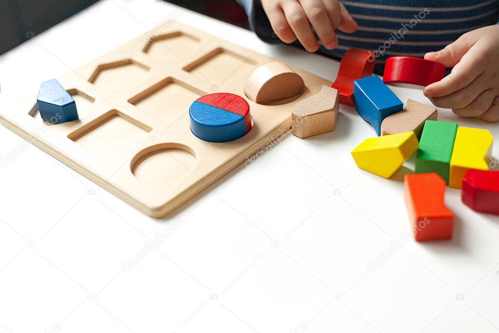 Educational toys, Cognitive skills, Montessori activity. Closeup: Hands of a little Montessori kid learning about color, shape, sorting, arranging by engaged colorful wooden sensorial blocks.