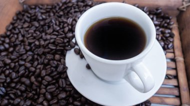 Beyaz kahve fincanıyla ahşap bir fonda siyah kahve çekirdeklerini kapat..