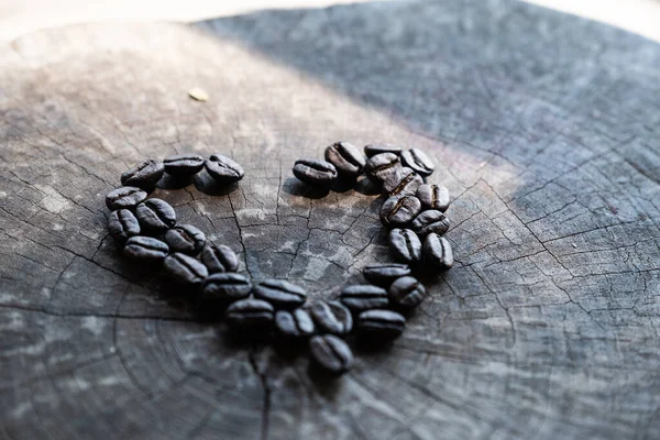 Siyah Kahve Çekirdeklerini Kapatır Güneş Gölgelerindeki Ahşap Arka Planda Kalp — Stok fotoğraf