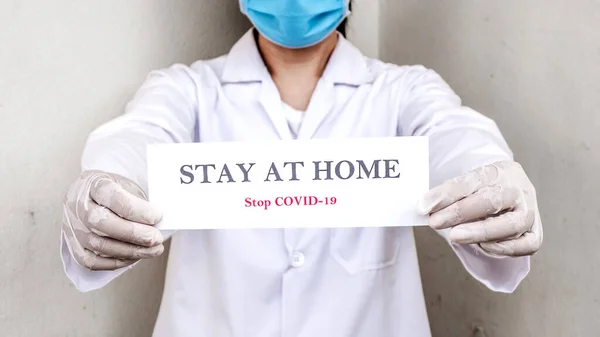 Bir doktor, insanları evlerinde güvende kalmaları için motive eden bir tabela tutuyor. Coronavirüs veya Covid-19 salgınından korunmak için.