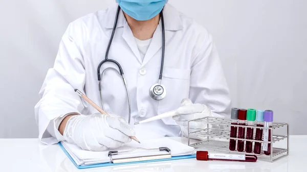 Bir doktor beyaz arka plandaki tüplerden alınan kan testlerini test ediyor.
