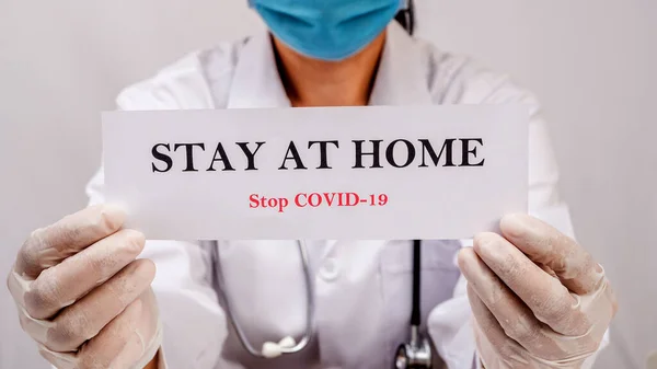Bir doktor, insanları evlerinde güvende kalmaları için motive eden bir tabela tutuyor. Coronavirüs veya Covid-19 salgınından korunmak için.