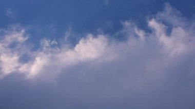 Kümülüs beyaz bulutlar mavi gökyüzünde hareket ediyor ve havada kayboluyor.